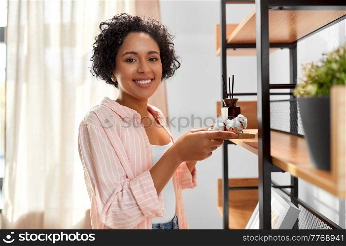 home improvement, decoration and people concept - happy smiling woman holding board with aroma reed diffuser and cotton flower at shelf. woman with aroma reed diffuser and cotton at home