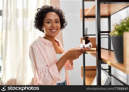 home improvement, decoration and people concept - happy smiling woman holding board with aroma reed diffuser and cotton flower at shelf. woman with aroma reed diffuser and cotton at home