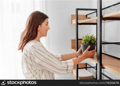 home improvement, decoration and people concept - happy smiling woman placing flower or houseplant to shelf. woman decorating home with flower or houseplant