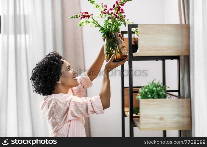 home improvement, decoration and people concept - happy smiling woman placing flowers to shelf. woman putting flowers on shelving at home