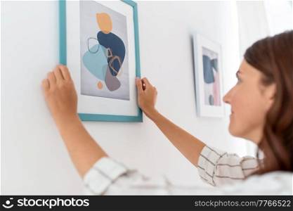 home improvement, decoration and people concept - woman hanging picture in frame on wall. woman decorating home with picture in frame