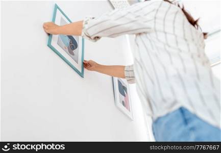 home improvement, decoration and people concept - woman hanging picture in frame on wall. woman decorating home with picture in frame