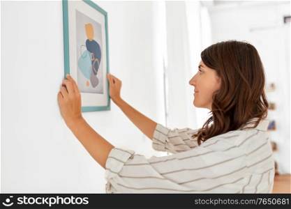 home improvement, decoration and people concept - woman placing picture in frame to wall. woman decorating home with picture in frame