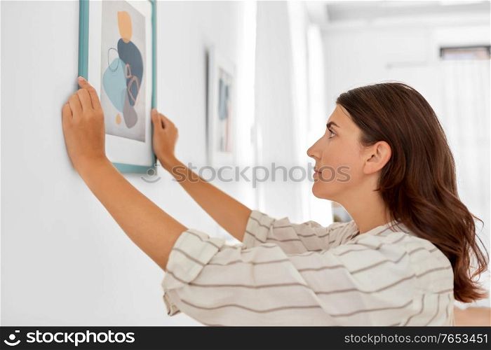 home improvement, decoration and people concept - woman placing picture in frame to wall. woman decorating home with picture in frame