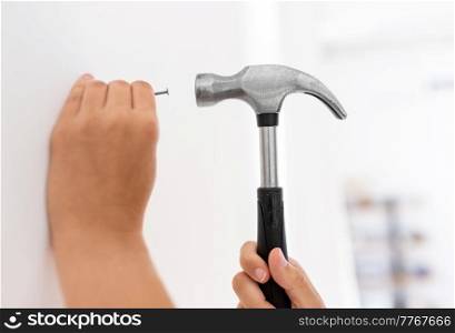 home improvement, repair and people concept - close up of hands hammering nail to wall. close up of hands hammering nail to wall at home