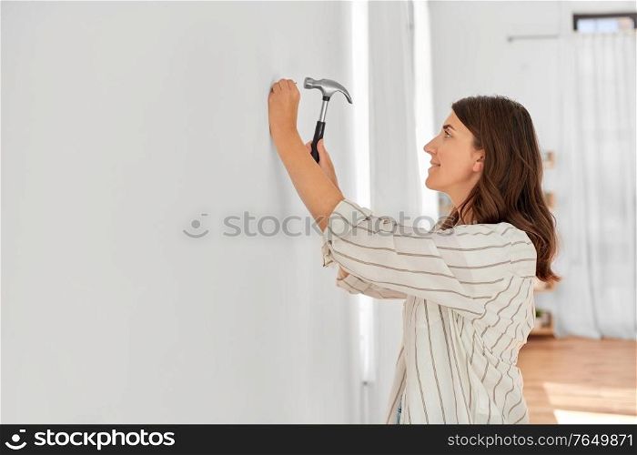 home improvement, repair and people concept - happy smiling woman hammering nail to wall. woman hammering nail to wall at home