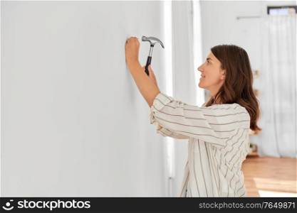 home improvement, repair and people concept - happy smiling woman hammering nail to wall. woman hammering nail to wall at home