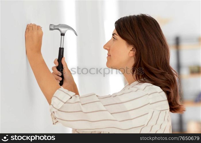 home improvement, repair and people concept - woman hammering nail to wall. woman hammering nail to wall at home