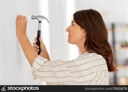 home improvement, repair and people concept - woman hammering nail to wall. woman hammering nail to wall at home