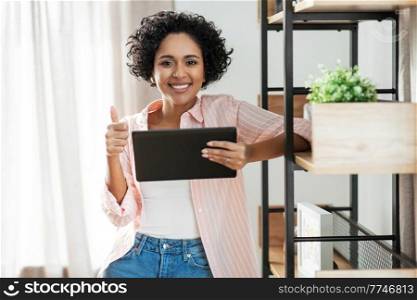 home improvement, technology and people concept - happy smiling woman with tablet pc computer standing at shelf and showing thumbs up. woman with tablet pc showing thumbs up at home