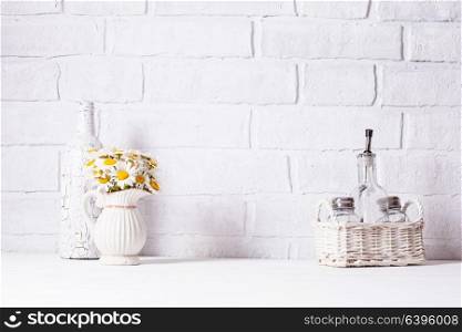 Home interior decoration, bouquet of daisies in white vase, decorative white bottle and glass bottle of oil in a basket. Home interior decoration