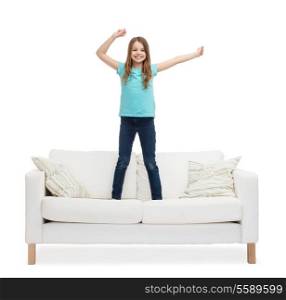 home, leisure and happiness concept - smiling little girl jumping or dancing on sofa