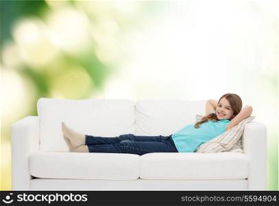home, leisure and happiness concept - smiling little girl lying on sofa