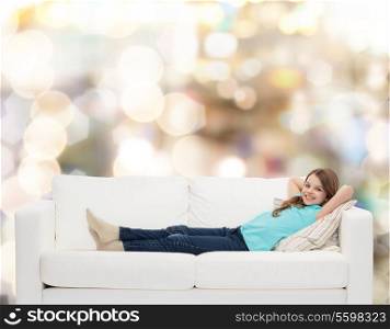 home, leisure and happiness concept - smiling little girl lying on sofa