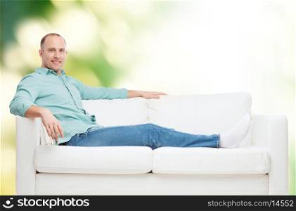 home, leisure and happiness concept - smiling man lying on sofa