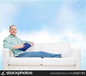 home, leisure and happiness concept - smiling man lying on sofa with book