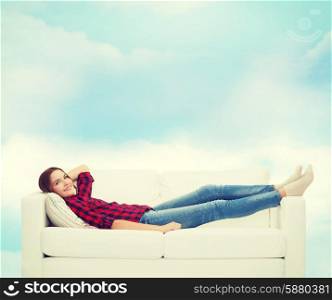 home, leisure and happiness concept - smiling teenage girl lying on sofa