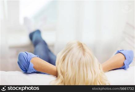 home, leisure and happiness concept - young woman lying or sitting on sofa at home