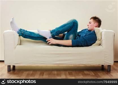 Home, leisure concept. Young handsome man relaxing on couch put on socks