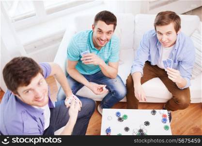 home, leisure, games, friendship, gambling and entertainment - three smiling male friends playing cards at home