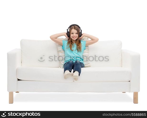 home, leisure, music and happiness concept - smiling little girl in headphones sitting on sofa