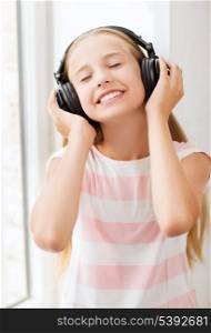 home, leisure, new technology and music concept - little girl with headphones at home