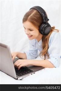 home, leisure, new technology and music concept - smiling little girl with laptop computer and headphones at home