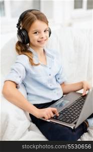 home, leisure, new technology and music concept - smiling little girl with laptop computer and headphones at home