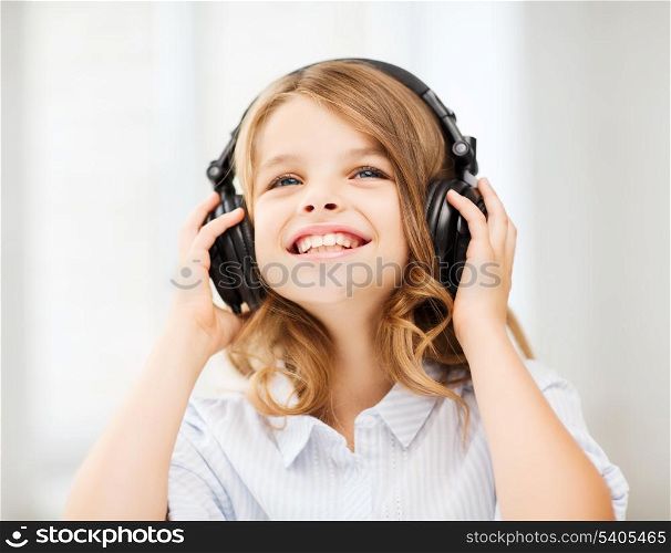 home, leisure, new technology and music concept - smiling little girl with headphones at home