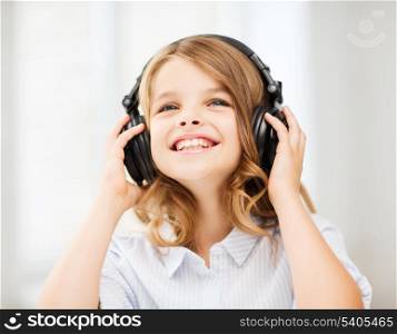 home, leisure, new technology and music concept - smiling little girl with headphones at home