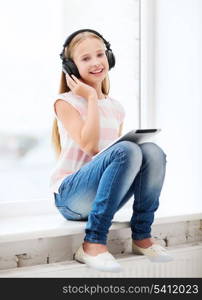 home, leisure, new technology, music concept - little girl with tablet pc and headphones at home