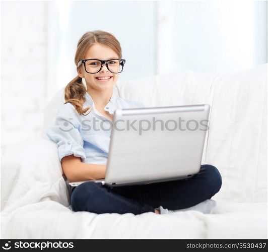 home, leisure, technology and internet concept - little student girl in eyeglasses with laptop computer at home