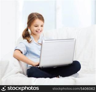 home, leisure, technology and internet concept - little student girl with laptop computer at home