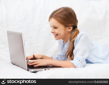 home, leisure, technology and internet concept - little student girl with laptop computer at home