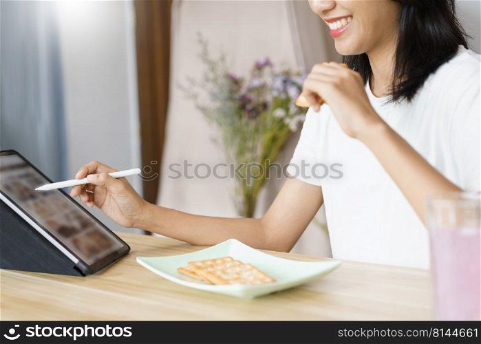 Home lifestyle concept, Young woman using tablet and eating crackers while leisure at home.