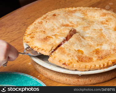 Home made baked fruit pie from oven and on table being cut with knife