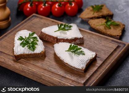 Home made bread on a wooden cutting board with curd cheese and ricotta and herbs. Sliced bread with cream cheese and butter for breakfast