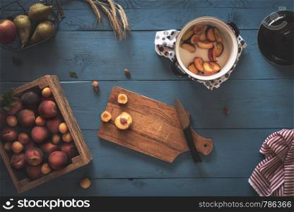Home making of peaches and apricot marmalade with a box of fresh fruits, sliced pieces in a pot, on a blue kitchen table. Above view with jam cooking.