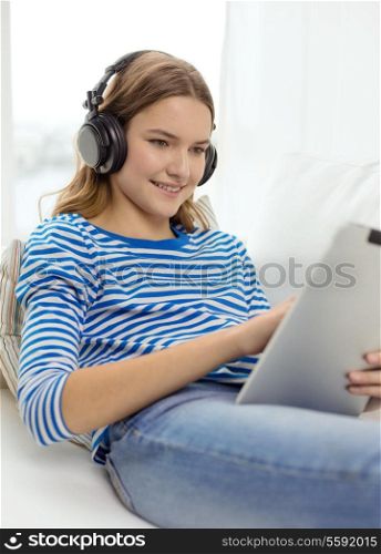 home, music, technology and internet concept - smiling teenage girl lying on the couch with tablet pc computer and headphones at home