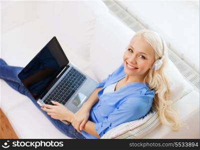 home, music, technology and internet concept - smiling woman lying on the couch with laptop computer and headphones at home