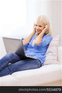 home, music, technology and internet concept - smiling woman lying on the couch with laptop computer and headphones at home