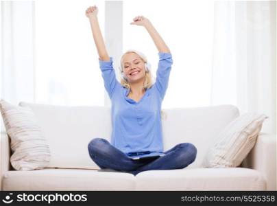 home, music, technology and internet concept - smiling woman sitting on the couch with tablet pc computer and headphones at home