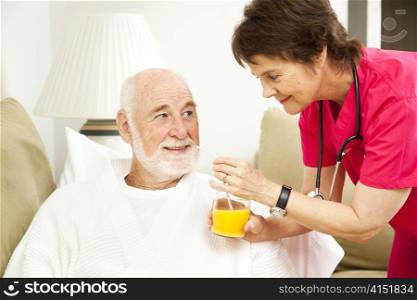 Home nurse giving her elderly patient a glass of orange juice.