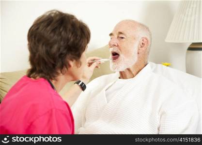 Home nurse uses a thermometer to take an elderly patient&rsquo;s temperature.