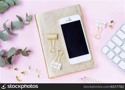 Home office desk with phone. Home office desk with green eucaliptus and modern white phone on pink background