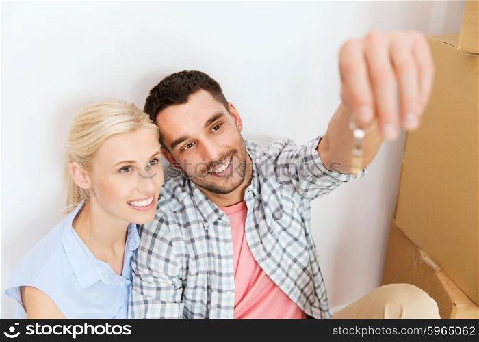 home, people and real estate concept - happy couple with key and cardboard boxes moving to new place