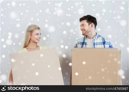 home, people and real estate concept - smiling couple with big cardboard boxes moving to new place over snow