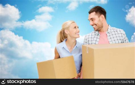 home, people, delivery and real estate concept - happy couple holding cardboard boxes over blue sky and clouds background