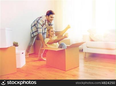 home, people, moving and real estate concept - happy couple having fun and riding in cardboard boxes at new home