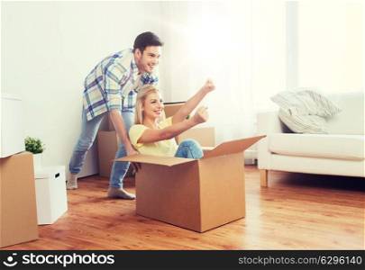 home, people, moving and real estate concept - happy couple having fun and riding in cardboard boxes at new home. happy couple having fun with boxes at new home